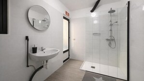 Un baño moderno con un espejo redondo, un lavabo blanco y una ducha con mampara de vidrio.
