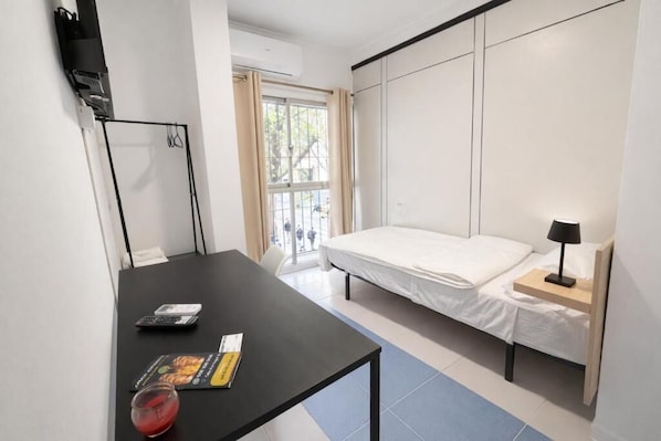 Un dormitorio con cama, mesita de noche, lámpara y ventana con cortinas.