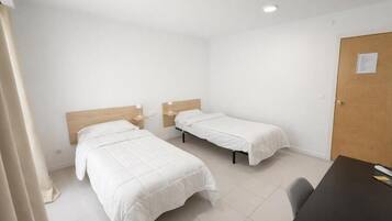Una habitación con dos camas, una puerta de madera y una mesa con una silla.