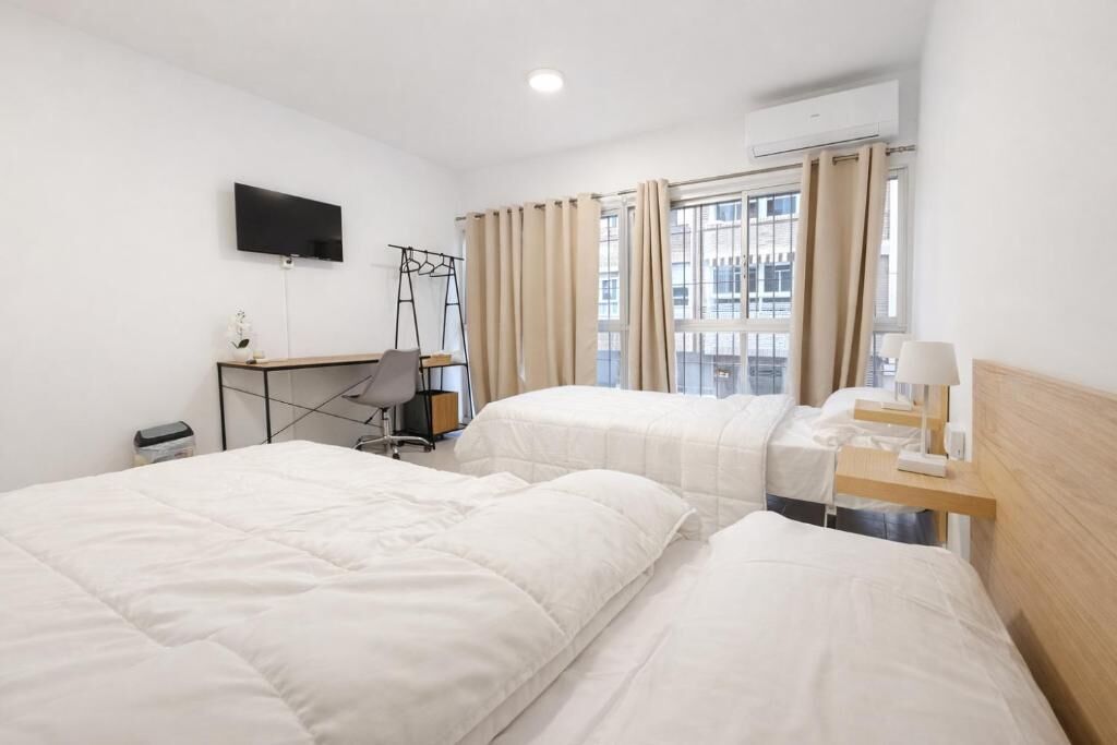 Habitación de hotel con dos camas, un escritorio, una silla, un televisor y una ventana con cortinas.