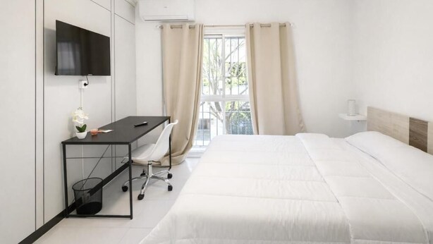 Una habitación de hotel con cama, escritorio con silla, televisor montado en la pared y ventana con cortinas.