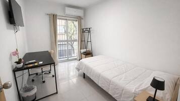 Habitación de hotel con cama, escritorio con silla, televisor montado en la pared, ventana con cortinas y un equipo de aire acondicionado.