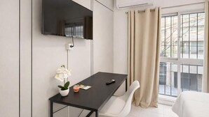 Una habitación de hotel moderna con un televisor de pantalla plana montado en la pared, una mesita con un jarrón de flores, un control remoto y una ventana con cortinas.