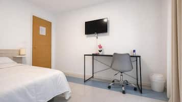 A hotel room with a bed, a desk with a chair, a television, and a trash bin.