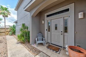 A house with a white door, a welcome mat, a potted plant, and a chair outside.