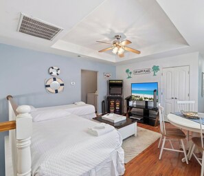 A bedroom with two beds, a ceiling fan, a TV, a small table, and a door.