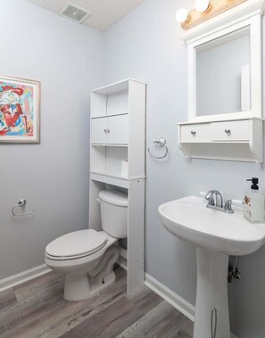Une salle de bain équipée d’un WC, d’un lavabo, d’un miroir et d’une étagère.