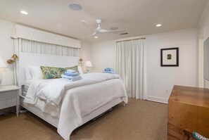 Ein Schlafzimmer mit Bett, Nachttischlampen, Deckenventilator und einem Holznachttisch.