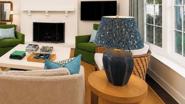 Een woonkamer met een beige bank, groene fauteuils, een salontafel met boeken, een open haard en een televisie aan de muur.