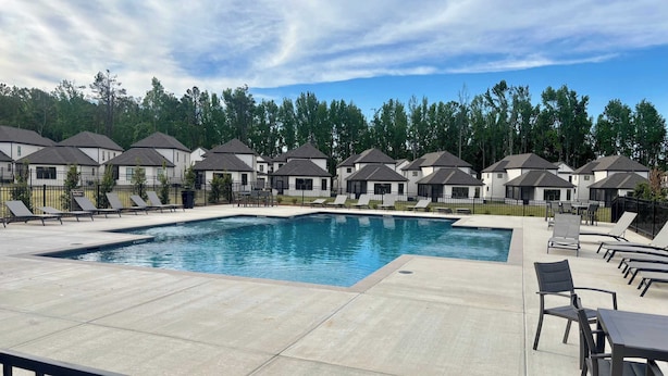 A swimming pool with lounge chairs and tables, surrounded by houses with similar architecture. - Hemingway Haven (Oxford)