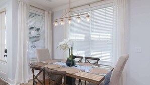 A dining area with a table set for four, surrounded by chairs, with a vase of flowers on the table. - Hemingway Haven (Oxford)