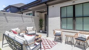 A patio with outdoor furniture, a potted plant, and a view of a building with large windows. - Hemingway Haven (Oxford)