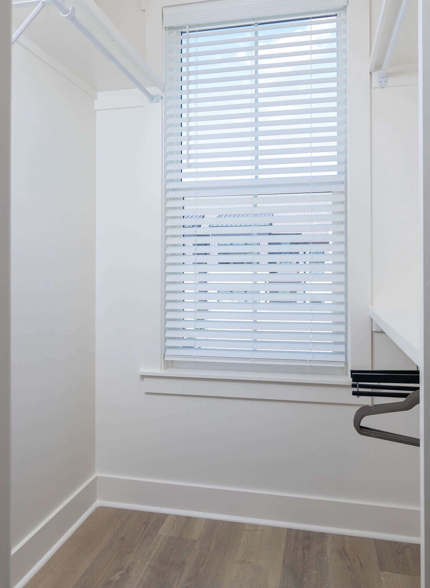 A room with a window, wooden flooring, and white walls.