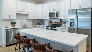 A modern kitchen with white cabinets, stainless steel appliances, and a central island with bar stools. - Hemingway Haven (Oxford)