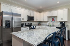 A kitchen with white cabinets, stainless steel appliances, granite countertops, and blue bar stools. - Hotty Toddy Hideout (Oxford)