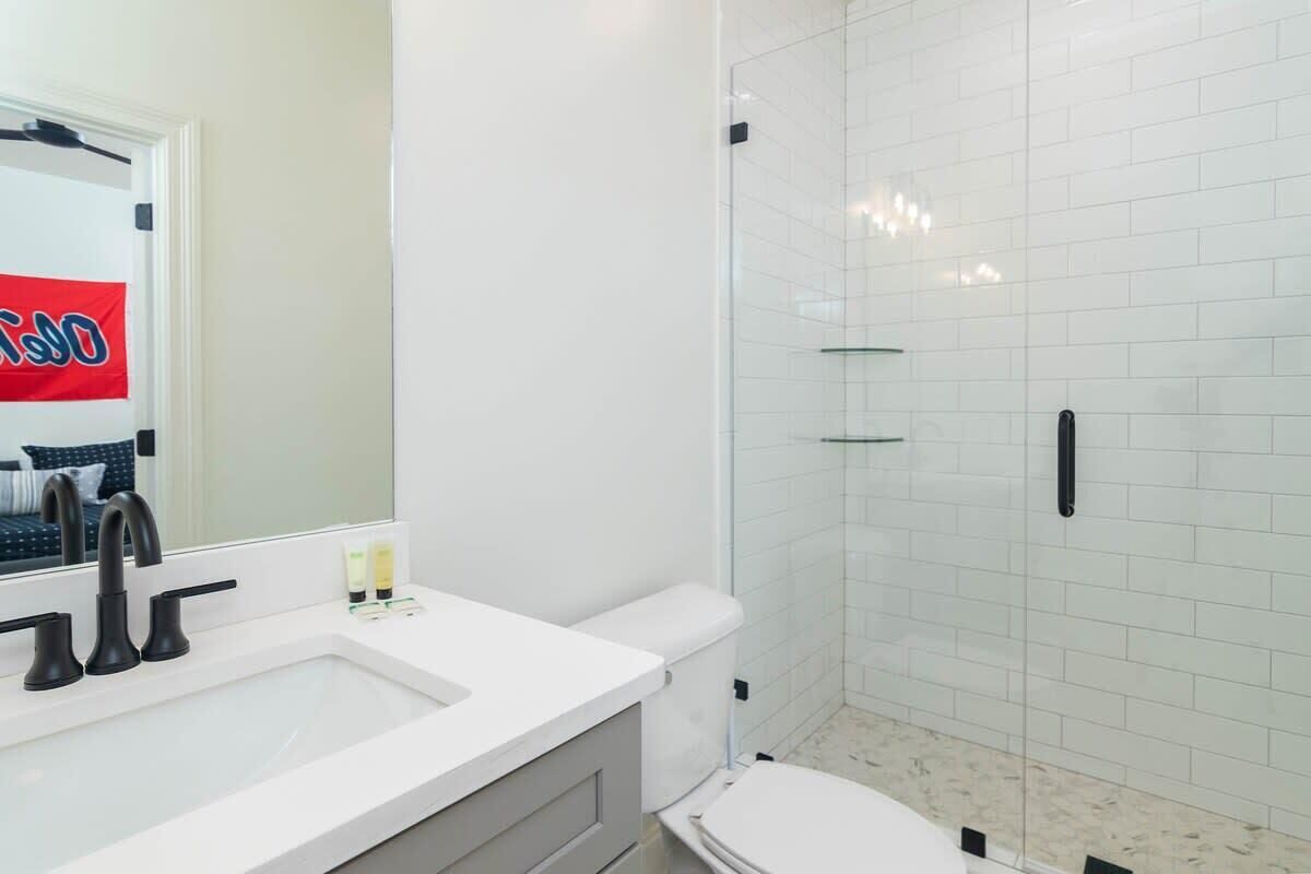 Ein modernes Badezimmer mit einem weißen Waschbecken, schwarzen Armaturen, einer Toilette und einer Duschkabine aus Glas.