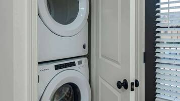 Una sala de bugaderia amb dues rentadores frontals blanques, una porta amb mànega negra i una finestra amb persianes.