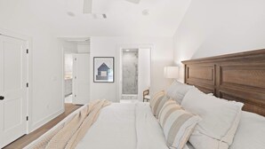 Camera da letto con un letto grande, una testiera in legno, una ventola a soffitto e una porta che dà su un bagno.
