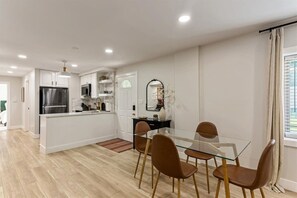 Una cocina moderna con armarios blancos, un refrigerador de acero inoxidable y una mesa de comedor de vidrio con cuatro sillas.