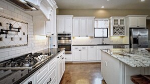 Una cocina con armarios blancos, un refrigerador de acero inoxidable y una encimera de mármol.