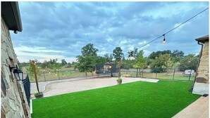 Un patio con césped artificial verde, un muro de piedra y una valla de metal.