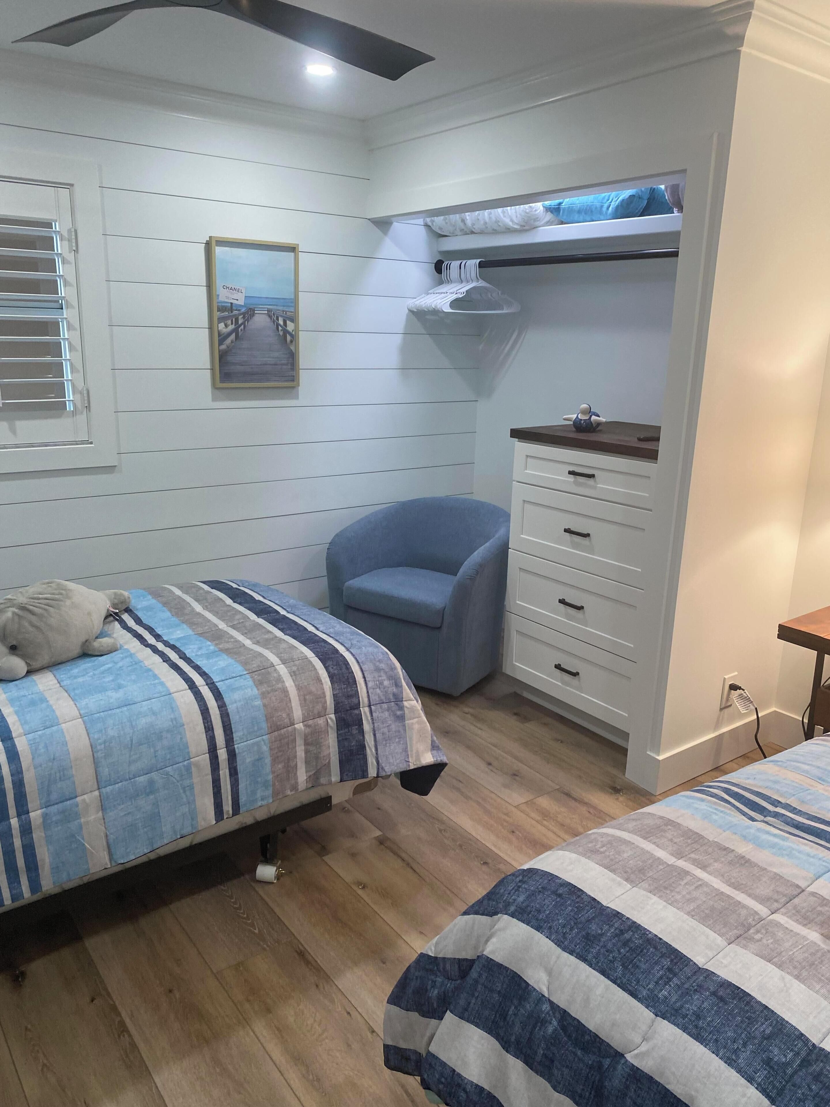 A bedroom with two beds, a chair, a dresser, a bunk bed, and a wall-mounted shelf.