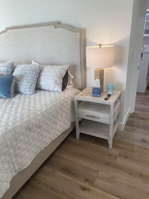 Ein Bett mit Kopfteil, ein Nachttisch mit Lampe, einer Fernbedienung und einer Taschentuchbox.
