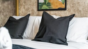 Uma cama com almofadas brancas e pretas, um cobertor escuro e um quadro na parede.