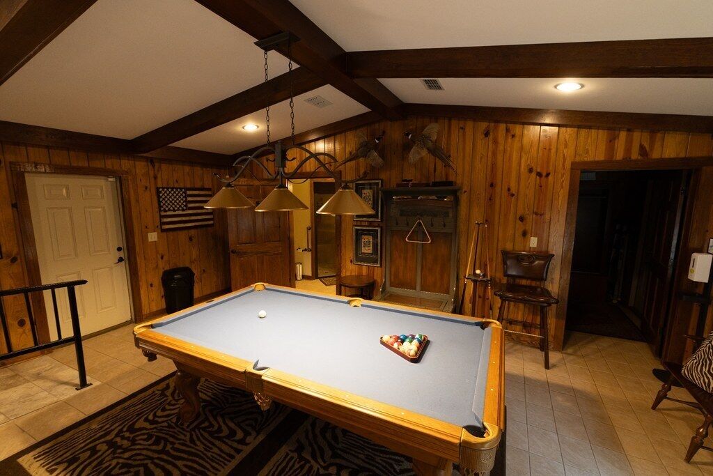 A pool table in a room with wooden walls, a zebra-patterned rug, and a hanging lamp.