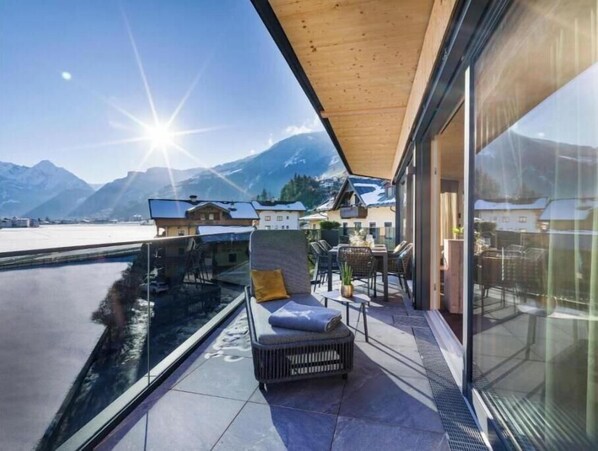Eine moderne Terrassenanlage im Freien mit Blick auf Berge und einen See, ausgestattet mit einer Couch und einem Esstisch.