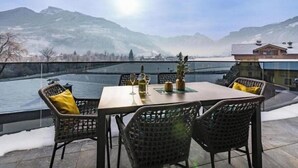 A table with chairs and a bottle of wine on a terrace overlooking a river and mountains. - Stylish feel-good apartments with sauna & mountain views in Zillertal (Zellbergeben)