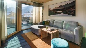 En moderne stue med sofa, sofabord og et stort vindue med udsigt til bjerge.