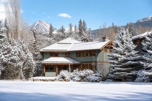 Eine zweistöckige Lodge mit einer markanten Veranda, umgeben von schneebedeckten Bäumen und Bergen im Hintergrund.