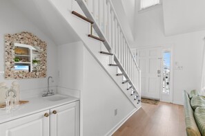 Eine Treppe mit weißer Handläufe, ein Küchenbereich mit weißen Schränken und ein grünes Sofa.