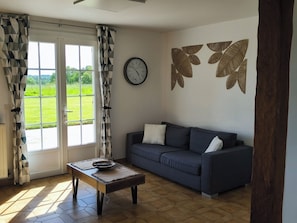 Un salon avec un canapé, une table basse, une horloge murale et une fenêtre avec des rideaux.