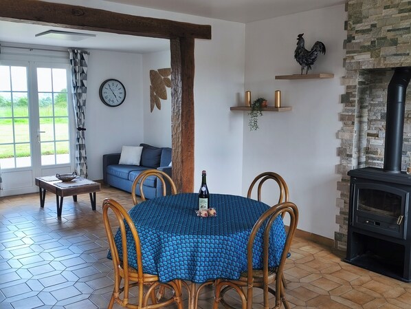 Un coin repas avec une table ronde, des chaises, une horloge, un canapé, une cheminée et une vue à travers une porte vitrée.