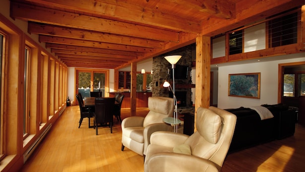 Una habitación amplia con techo de madera, chimenea de piedra, zona de comedor con mesa y sillas, y espacio de estar con sofás.