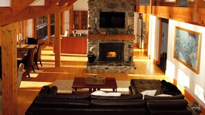 Un salón amplio con chimenea de piedra, vigas de madera, un sofá de cuero y un comedor con mesa y sillas de madera.