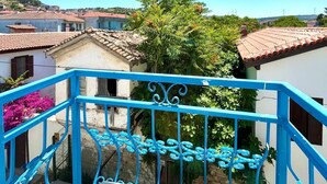 Un balcón con barandillas azules que da a una zona residencial con tejados de teja y un árbol.