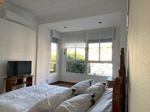 A bedroom with two beds, a TV on a wooden stand, and a window with blinds. - Rooms in plaza de toros in alicante Spain (Alacant)