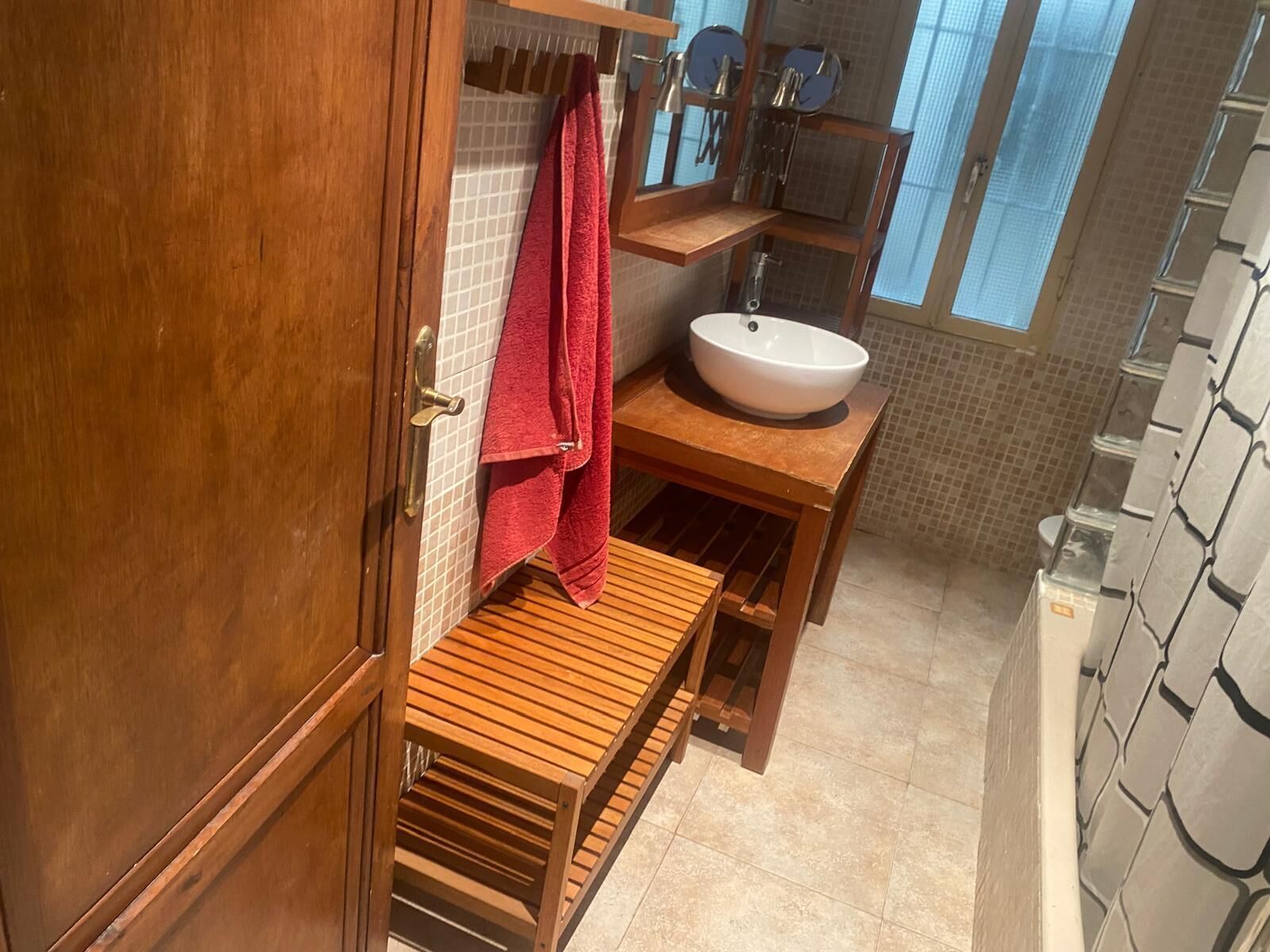 A bathroom with a wooden bench, a sink, and a red towel hanging on the wall.