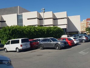 A parking lot with several cars, a modern building with a flat roof and large windows, and a clear blue sky. - Rooms in plaza de toros in alicante Spain (Alacant)
