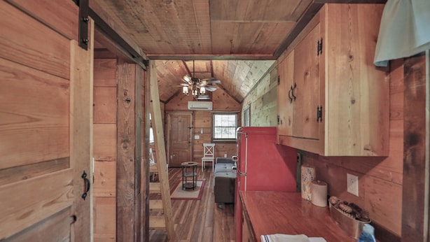 Interior de uma cabana de madeira com cozinha, mesa de jantar e ventilador de teto.