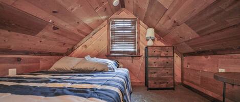 Um quarto de sótão pequeno e acolhedor, com teto inclinado, uma cama de solteiro, cômoda, abajur e janela com persianas.