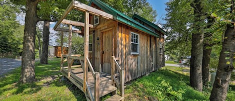 A wooden cabin with a porch and a green roof, surrounded by trees.