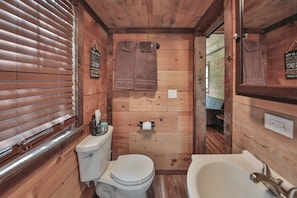 Ein kleines, hölzernes Badezimmer mit Toilette, Waschbecken und Handtuchhalter.