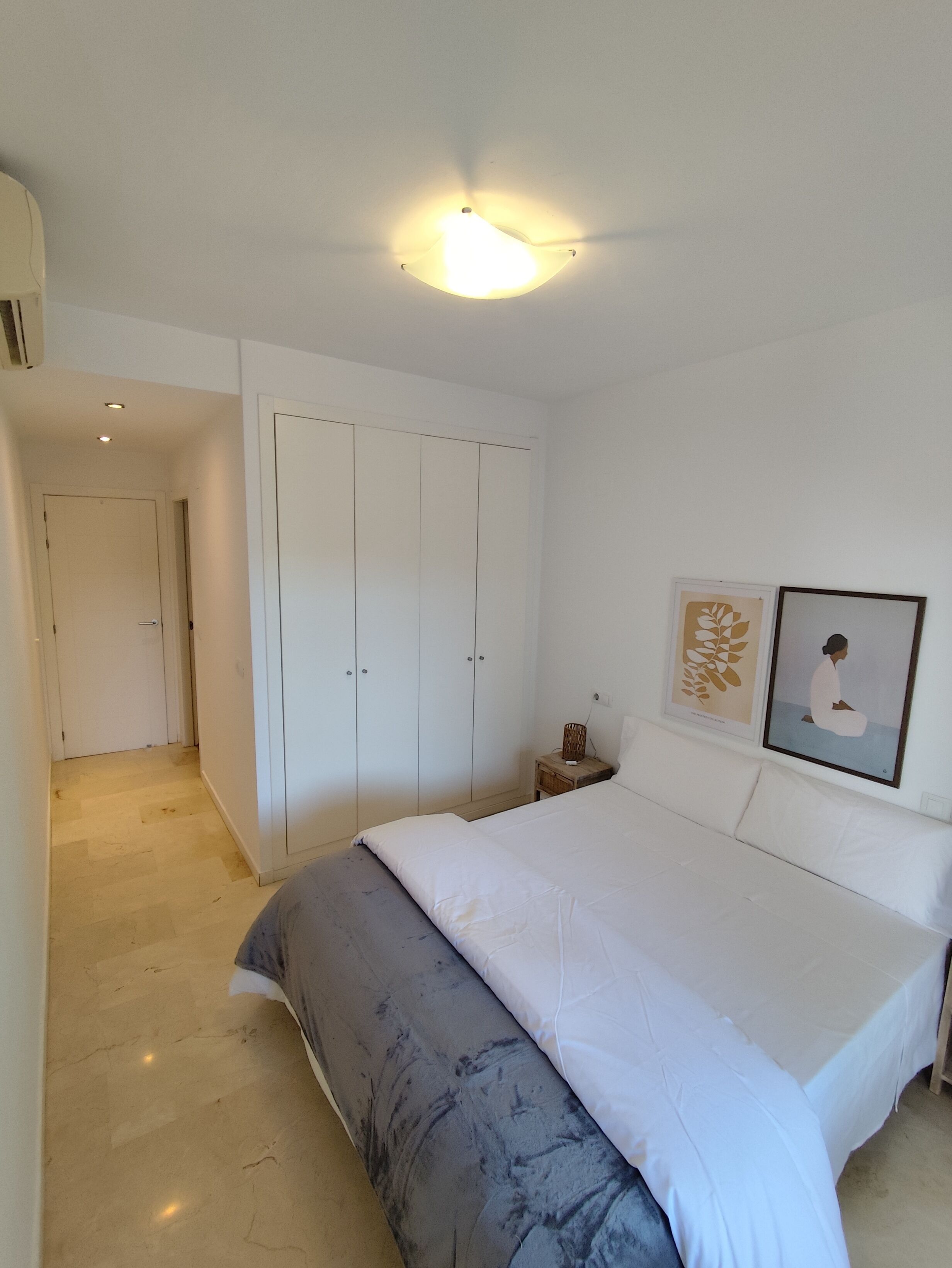 A bedroom with a bed, a wardrobe, a nightstand, and a framed picture on the wall.