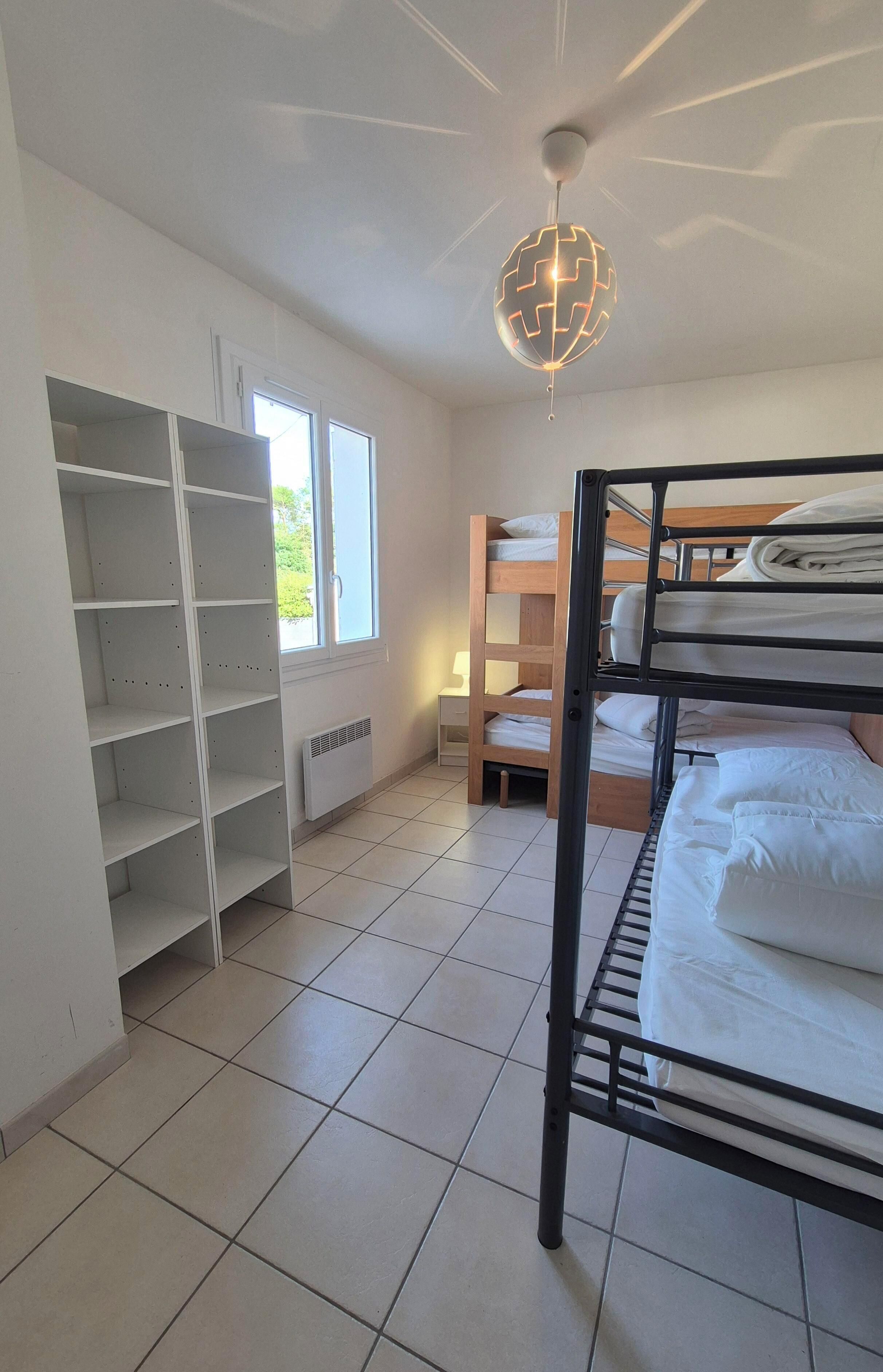 Een kamer met stapelbedden, een witte garderobe, een radiator en een plafondlamp.