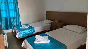 Hotellihuone, jossa on kaksi erillistä sänkyä, puinen pääty, yöpöytä, jossa on puhelin, ja ikkuna, jossa on verhot.