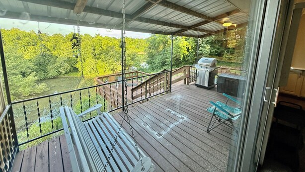 A covered deck with a grill, seating, and a view of a river and forest.